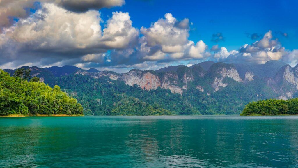 Cheow Lan Lake in Khao Sok National Park with emerald water and limestone karst cliffs under dramatic clouds