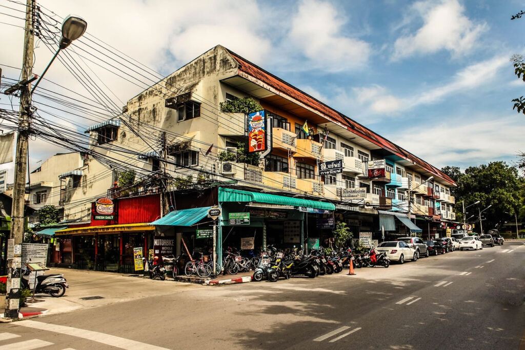 A typical street scene in Chiang Mai with local shops, motorbikes, and low-rise apartment buildings.