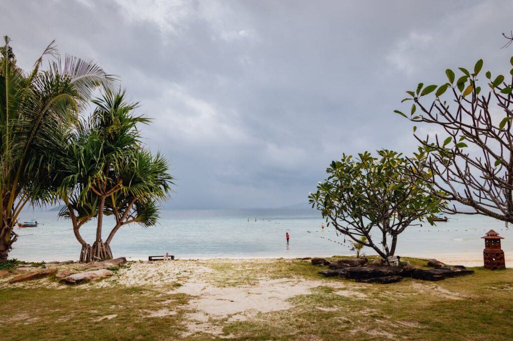 Calm beach in Thailand under cloudy sky with trees and shoreline in foreground