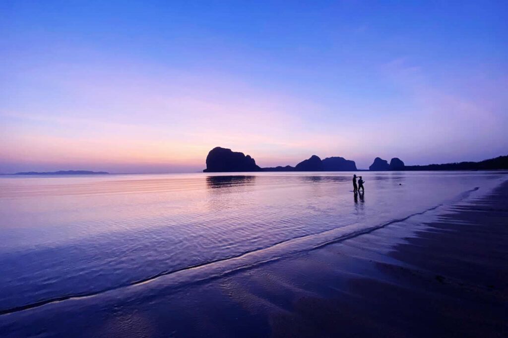 People walking along a quiet beach at twilight in Thailand symbolizing patience and long term thinking