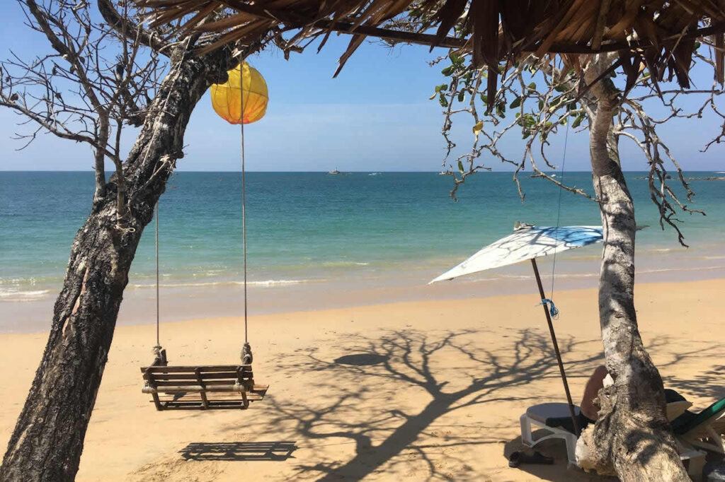 Wooden swing hanging from palm trees on a quiet beach in Thailand with calm turquoise sea