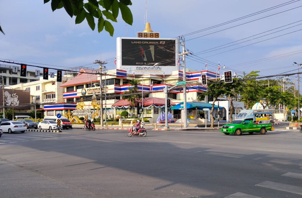 Hua Hin City Municipality building at a busy intersection with traffic lights, motorbikes, and a green songthaew taxi in Hua Hin, Thailand.