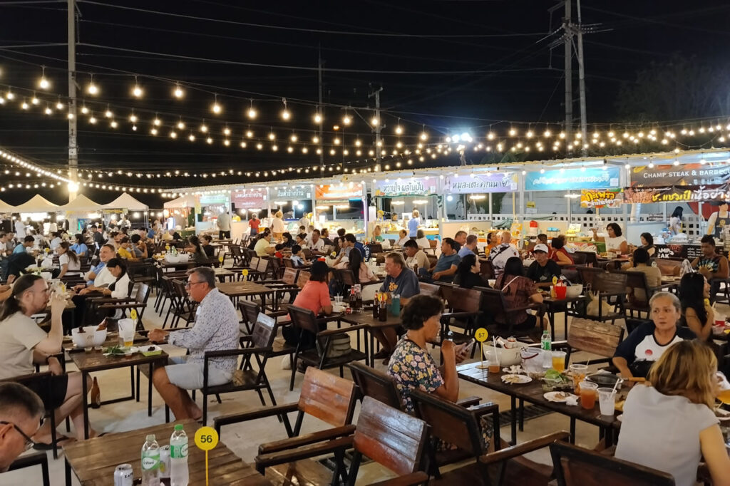 Busy open-air food court and night market in Hua Hin with diners, food stalls, and string lights in the evening.