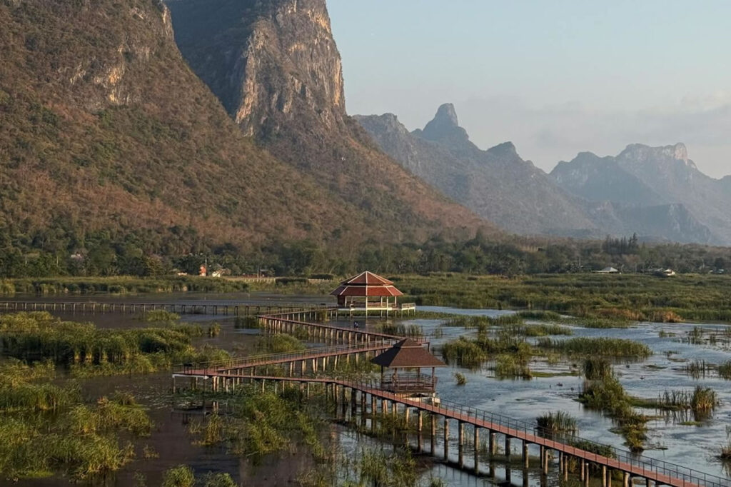 Wooden boardwalk and viewing pavilions across wetlands with dramatic limestone mountains in Sam Roi Yot National Park, Thailand.