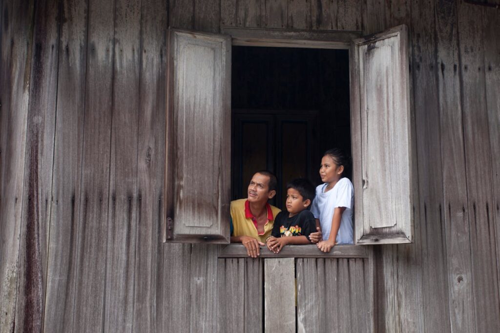 Thai family looking out from a wooden house window representing rural life and family ties in Isaan