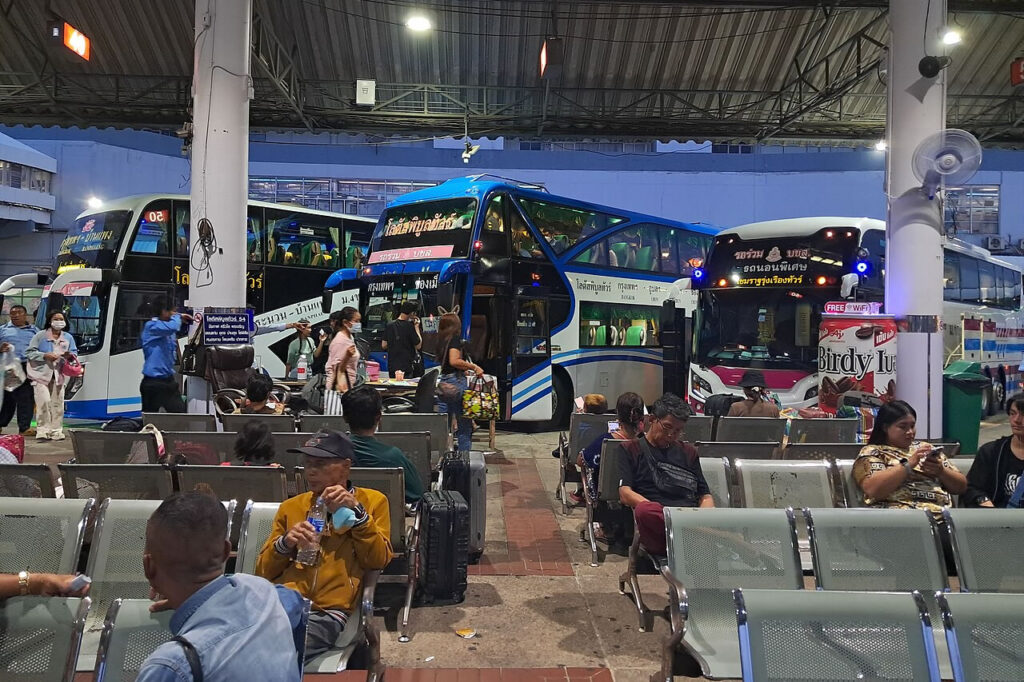 Passengers waiting at a Thai bus terminal with luggage showing everyday travel and migration in Thailand