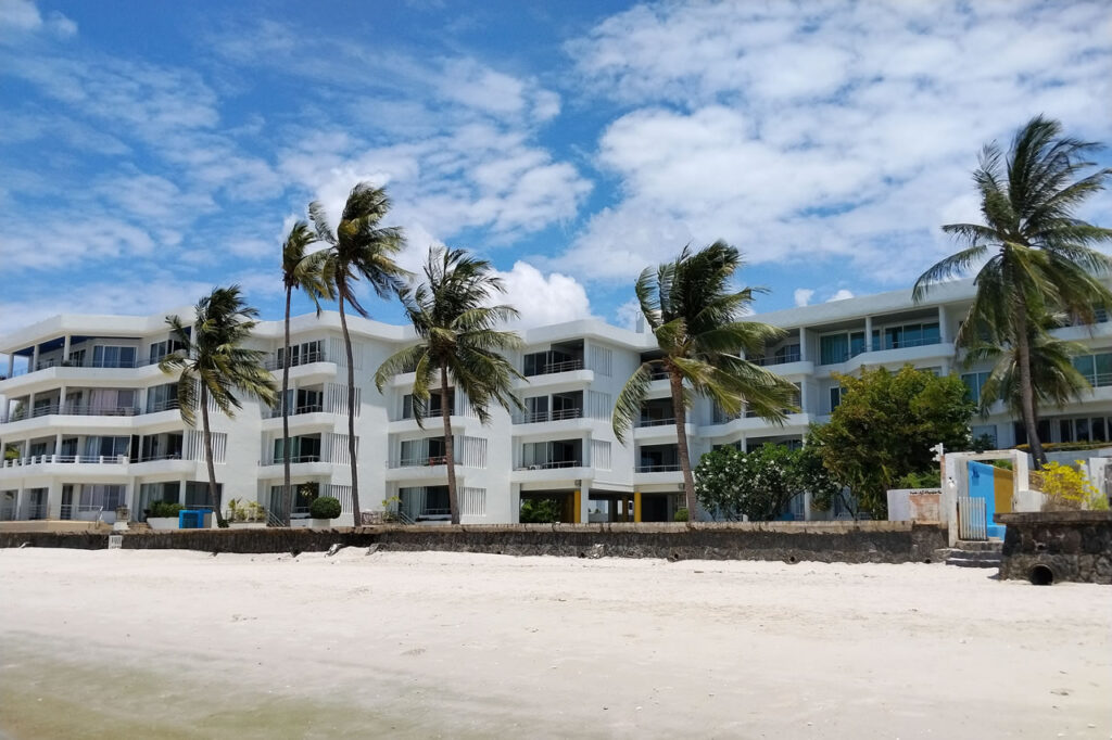 Beachfront condominium building in Hua Hin with palm trees and direct access to a sandy beach.