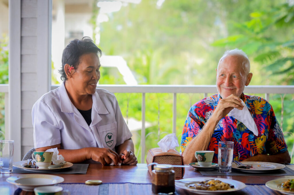 Caregiver sharing a meal with an elderly expat receiving home care support in Hua Hin, Thailand.