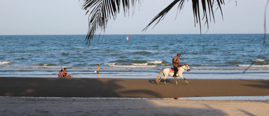 Horse rider on Hua Hin Beach with families enjoying the shoreline