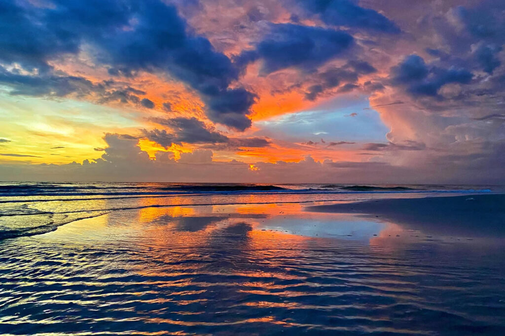 Sunrise over Hua Hin Beach with colorful clouds reflected across the wet sand along Thailandβs Gulf Coast.