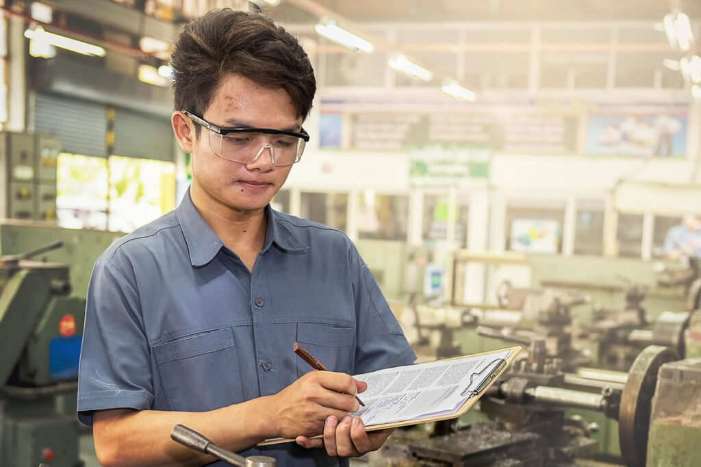 Thai factory worker in an industrial workshop, representing employment, household finances, and economic pressures in Thailand.