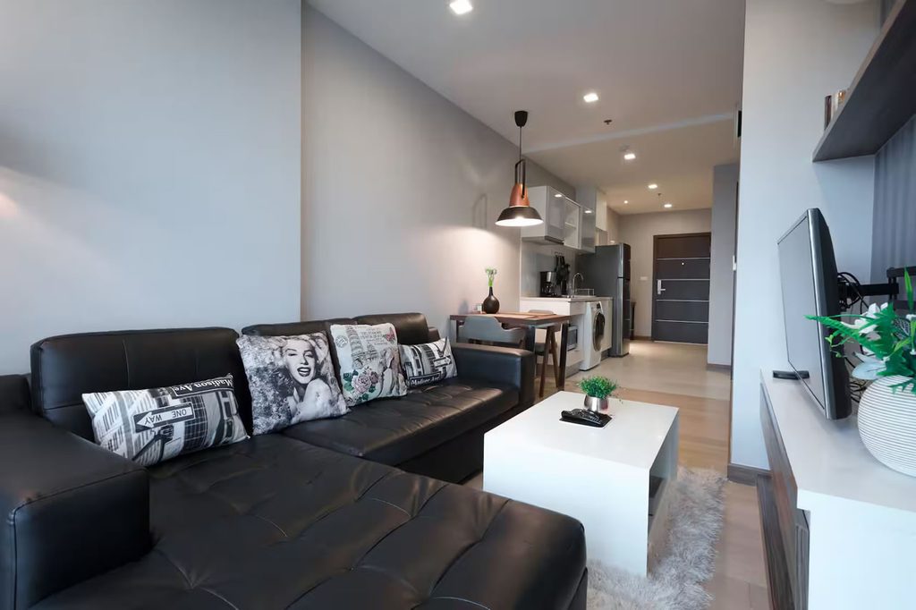 Living room with an L-shaped sofa, dining table and adjoining kitchen in a condo at The Astra, Chiang Mai