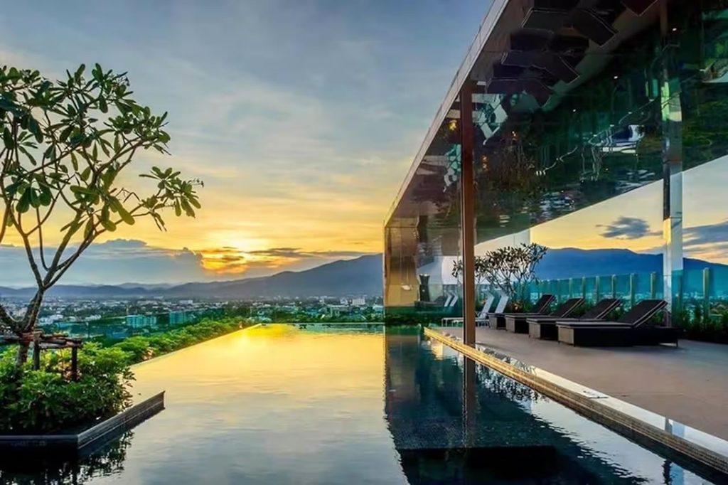 Rooftop swimming pool and sun loungers at The Astra condominium in Chiang Mai, overlooking the city and mountains at sunset