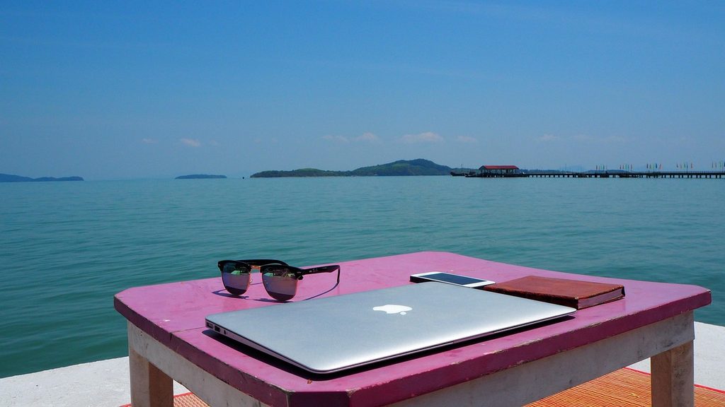 Laptop on a pink table overlooking the sea and a pier on Koh Lanta.