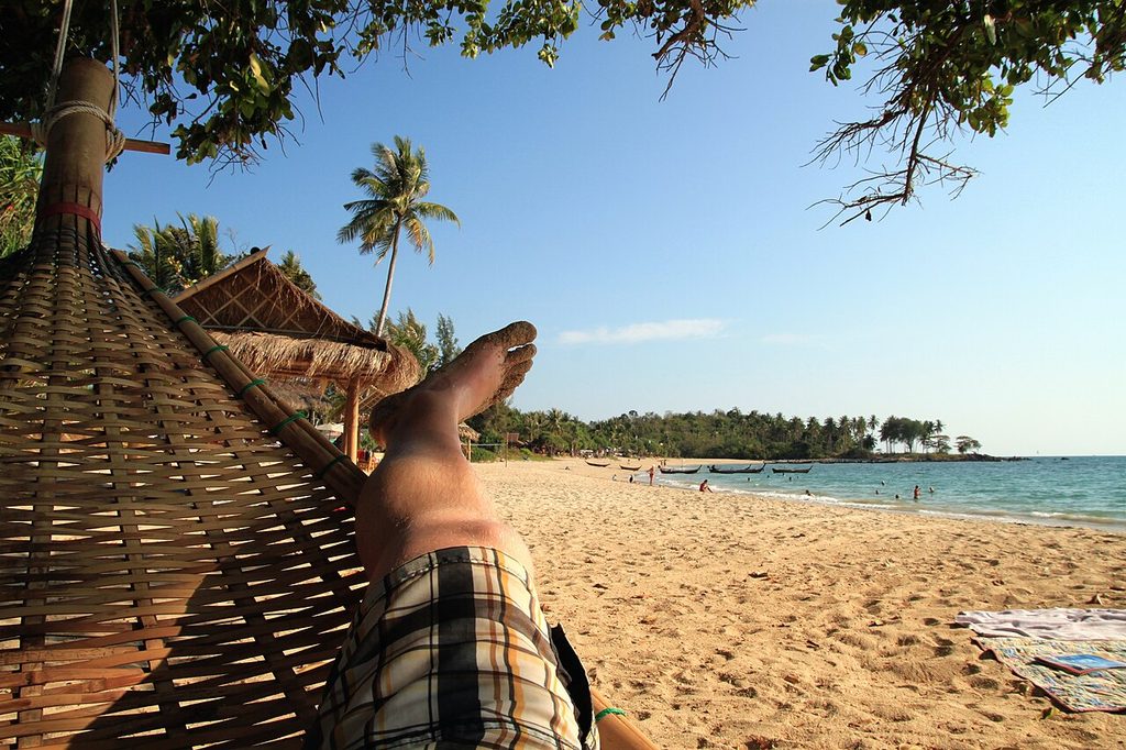 View from a hammock in the shade overlooking Relax Bay’s sandy beach, longtail boats and swimmers on Koh Lanta.