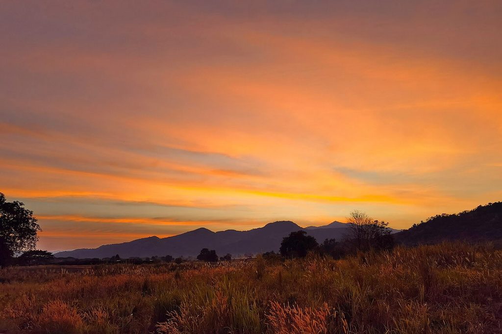 Orange sunset sky above grassland and silhouetted hills in Kui Buri National Park.